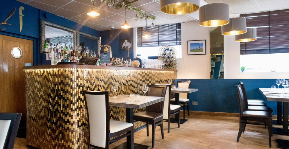 Modern restaurant interior with gold-tiled bar, blue walls, and neatly set tables. Modern restaurant interior with gold-tiled bar, blue walls, and neatly set tables.