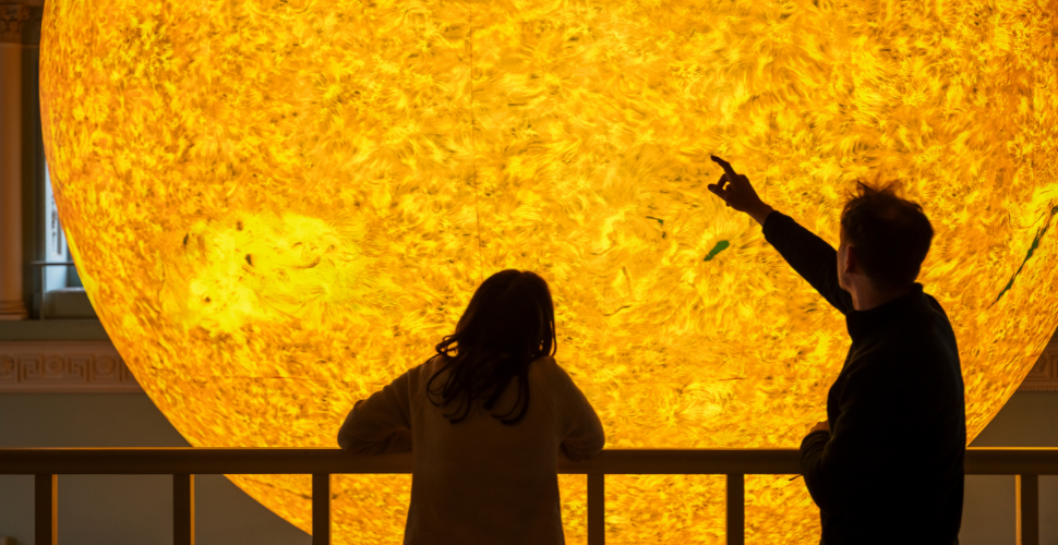 Two people point at an art installation of the sun