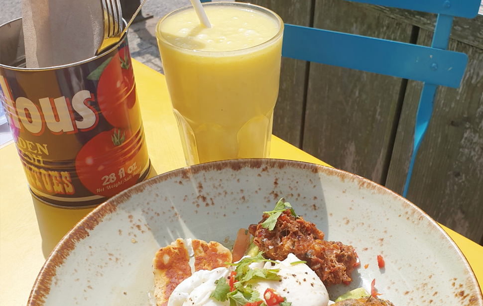 Spicy sweetcorn hash breakfast with a mango lassi drink sits on a yellow table at Boston Tea Party