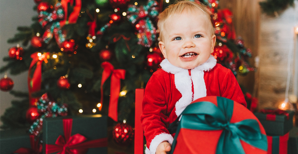 Baby holding a Christmas present in front of a Christmas tree
