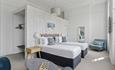 Chic hotel room with two single beds, white bedding, patterned pillows, and a wooden headboard. Includes a blue armchair, chessboard on a round table,